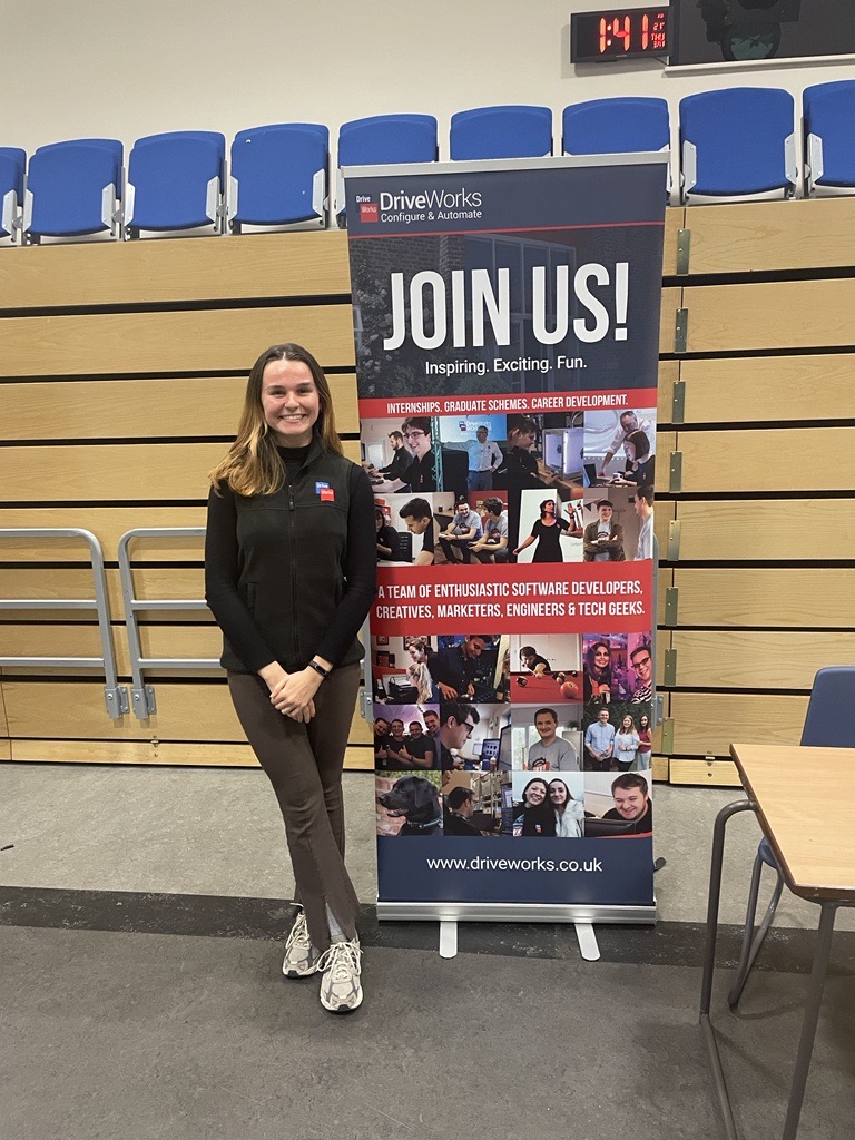 DriveWorks Placement Student Application Engineer, Chloe at a careers fayre with a 'join us' sign.
